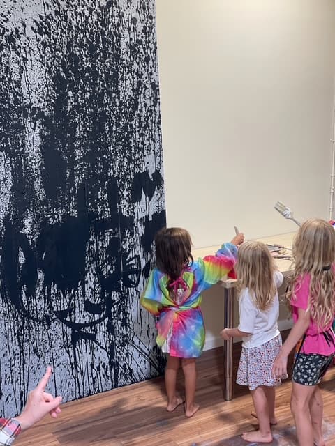 Three girls in smocks standing before a black-painted studio wall and a work table