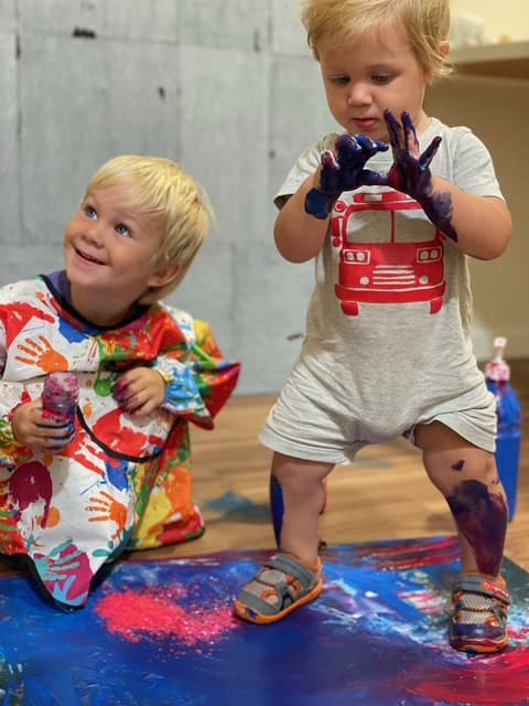 Two young children with purple paint on their hands, playing on a blue mat in the studio