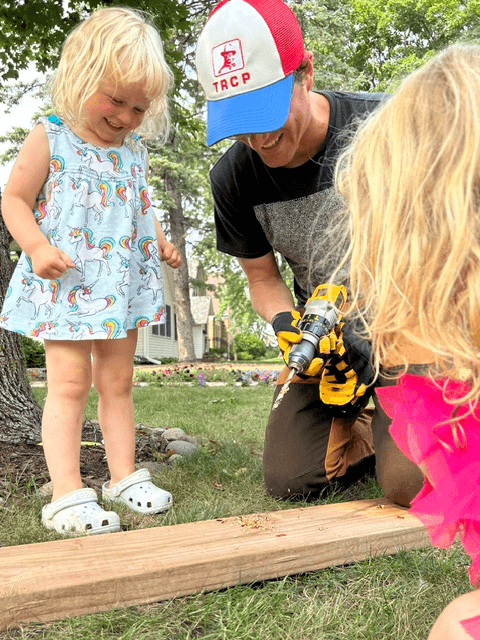 Michael Johnson working outdoors with a power drill alongside children.